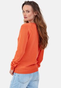 Pull en maille orange à manches longues, avec poignets et ourlet côtelés, porté avec un jean taille haute bleu clair, présentant une texture lisse.