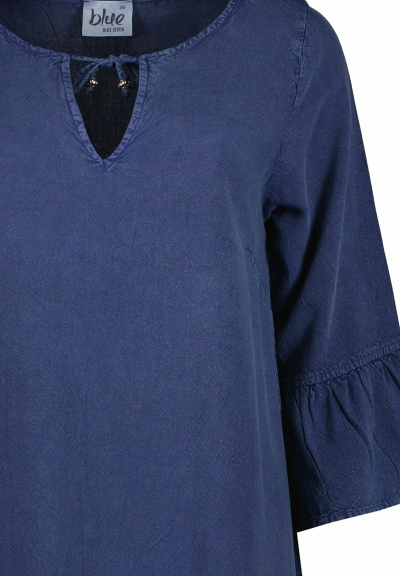 Blauw langlopende blouse met ronde halslijn, kleine sleufopening, stoffen strikjes met kralen en geplooide manchet op de mouwen.