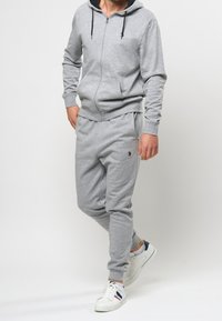 Harmaa vetoketjullinen hupullinen collegepaita mustilla nyöreillä, yhdistetty harmaisiin collegehousuihin, joissa on merkki. Yhdistetty valkoisiin lenkkareihin.