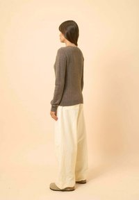 Szary dzianinowy sweter z teksturowanym wzorem, połączony z luźnymi białymi spodniami i szarym obuwiem. Tło jest w miękkim, neutralnym odcieniu.