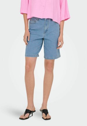 Ljusblå denimshorts med en avslappnad passform, som slutar strax ovanför knäet. Kombinerat med en rosa kort topp och svarta öppna klackar.