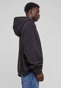 Sort bomulds hættetrøje med oversized pasform, faldne skuldre, ribbede ærmer og kant, parret med lyseblå denim jeans.