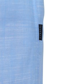 Helle blaue Stoff mit strukturierter Oberfläche. Enthält ein schwarzes Etikett an der Seite. Saubere Nähte entlang der Kanten. Lässiges Design.