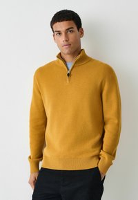 Maglione giallo senape con zip al collo e polsini e orlo a coste. Tessuto morbido, finitura liscia e zip di un quarto di lunghezza per un colletto regolabile.