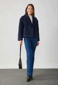 Navy wool-blend double-breasted jacket, cropped design with wide lapels, paired with blue straight-leg jeans and black ankle boots.