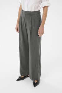Pantalon gris à rayures avec taille haute, devant plissé et jambes larges, associé à des ballerines noires pointues avec des accents de nœud.