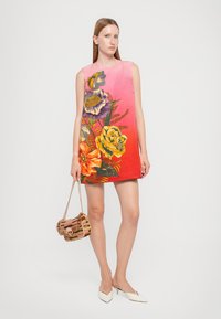 Sleeveless dress featuring a gradient from pink to red, adorned with colorful floral prints. Model holds a textured woven handbag.