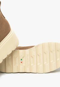 Bottines en daim marron avec une semelle texturée beige, présentant un design à plateforme et des détails de logo subtils sur la semelle.