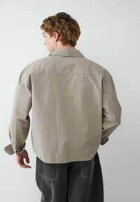 Braun- und cremefarbener karierthemd in entspannter Passform mit spitzen Kragen, Knopfmanschetten und Rückenpasse. Kombiniert mit dunkelgrauen Hosen.