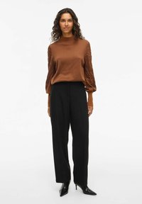 Pull marron avec des manches texturées et bouffantes, associé à un pantalon noir taille haute et des escarpins noirs pointus. Tricot lisse avec une coupe décontractée.