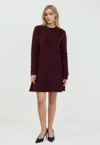 Burgunderfarbener Strickpullover und Faltenrock-Kombination. Der Pullover hat einen runden Ausschnitt und gerippte Bündchen, während der Rock einen ausgestellten Schnitt und Textur aufweist.