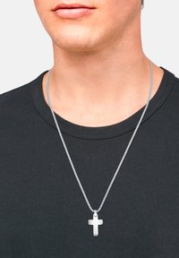 Collana in argento con un semplice pendente a croce, posata su una maglietta nera a girocollo. Texture liscia, design minimalista.