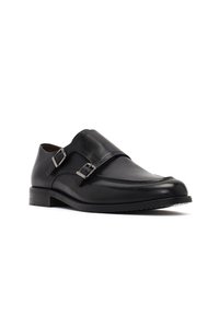 Zapato de vestir de cuero negro con punta redondeada, acentos de doble hebilla y parte superior lisa. Presenta un tacón bajo y apilado y una suela texturizada.