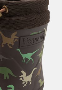 Hnedý gumený vedierko s obrysmi dinosaurov v zelenej a béžovej farbe, textúrovaný horný okraj so sieťovaným detailom a embosovaným logom.