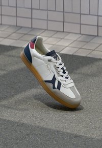 Weiße Sneaker mit marineblauen und roten Akzenten, ausgestattet mit einer Gummisohle, strukturiertem Zehenbereich und einem glatten Finish mit Schnürung.