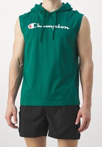 Zelená bezrukávová mikina vyrobená z bavlny, s přední kapsou, stahovací šňůrkou a bílým logem "Champion" přes hrudník.