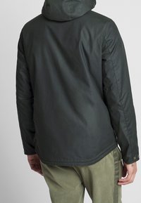 Dark green waterproof jacket with a hood, smooth texture, button accents on the cuffs, and a slightly longer back hem.