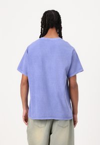 Camiseta de algodón lavanda de corte holgado y manga corta, con cuello redondo, costuras visibles y una silueta relajada.