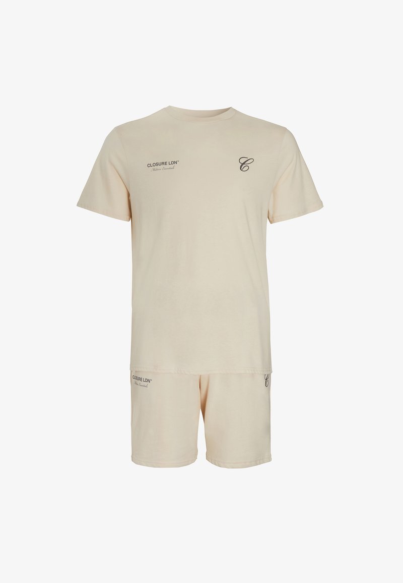 Set de îmbrăcăminte de lounge din bumbac, în nuanță bej deschis, cu mâneci scurte, format dintr-un tricou cu guler rotund și pantaloni scurți asortați, cu un branding subtil în text închis.