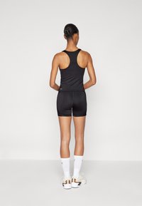 Sort atletisk top med racerback-design, parret med sorte shorts. Modellen har også hvide sokker og sportssko med teksturerede detaljer på.
