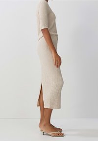 Beige texturerad stickad klänning med korta ärmar, längd till mitten av vaden, slits på sidan och platta sandaler med smal rem.