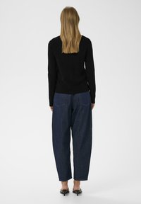 Svart ribbad tröja med långa ärmar, tillsammans med löst sittande, mörkblå denimjeans. Jeansen har bakfickor och en avslappnad passform.