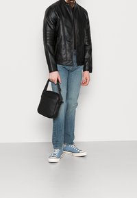 Chaqueta de cuero negra con detalles acanalados, jeans azul claro y zapatillas de lona azules. Se lleva un pequeño bolso negro en una mano.