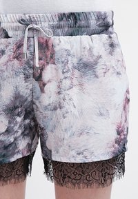 Kraťasy s květinovým vzorem v pastelových barvách s elastickým pasem a stahovací šňůrkou. Vystupuje černý krajkový lem podél lemu. Měkká textura.