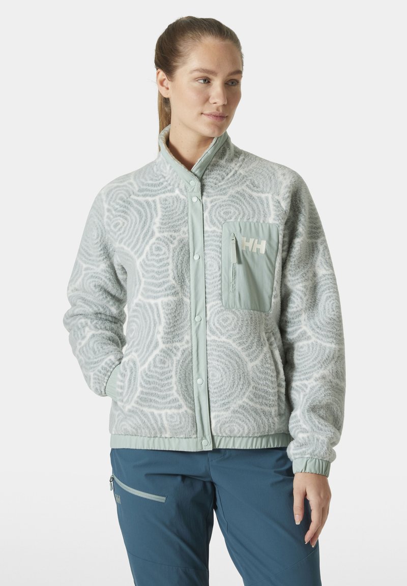 Jasnoszara polarowa kurtka z okrągłymi wzorami, wysoki kołnierz, zapięcie na napy z przodu oraz miętowozielona kieszeń zapinana na zamek z detalem logo.