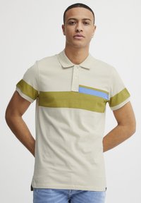 Beige polo-skjorte med grønne og blå horisontale striper, kortermet, og med en to-knapps placket laget av myk bomull.