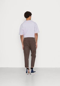 Liliowa koszulka z krótkim rękawem o luźnym kroju, zestawiona z brązowymi zwężanymi spodniami bojówkami z bocznymi kieszeniami oraz niebieskimi wysokimi trampkami.