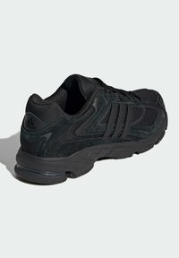Chaussure de sport noire en mesh et en cuir suédé. Elle présente une semelle intermédiaire texturée et un logo à trois rayures sur le côté. Design de talon arrondi.