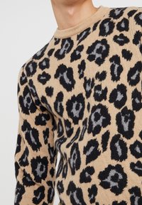 Beige tröja med svart och grå leopardmönster, rund halsringning, stickad textur, som visar en medelpassform och mönstrade detaljer.