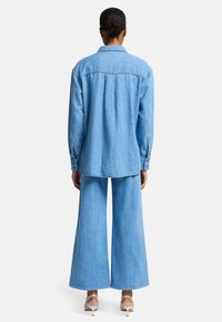 Jasnoniebieska koszula dżinsowa, z długim rękawem, z kołnierzykiem, o luźnym kroju. W zestawie ze spodniami o szerokich nogawkach w tym samym kolorze. Gładka tekstura, casualowy design.