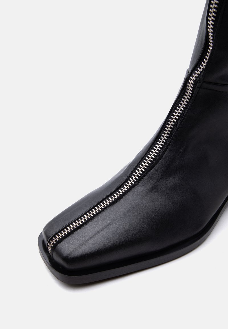 Black leather boot with a front silver zipper running from the toe to the ankle, square toe design, and flat sole.