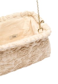 Beige stoffen tas met kralen, versierd met een textuurpatroon van bloemen, zachte bovenkant en een gouden schouderband. De binnenkant is eenvoudig met een zichtbaar label.