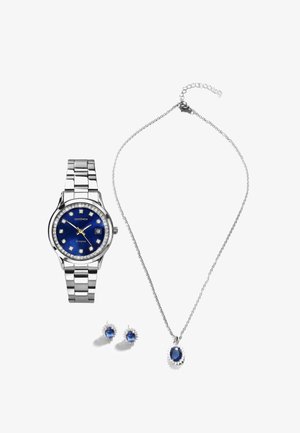 Montre en argent avec un cadran bleu et des accents en cristal, boucles d'oreilles bleues assorties et un collier avec un pendentif bleu sur une chaîne en argent.