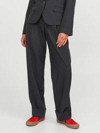 Schwarze, maßgeschneiderte Hose mit lockerer Passform, featuring ein flaches Vorderteil und hochgerollte Säume. Kombiniert mit roten Turnschuhen, die kontrastierende Farben zeigen.