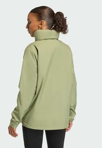 Svetlozelená vetrovka s vysokým golierom, dlhými rukávmi a elastickými manžetami, ktorá sa vyznačuje hladkou, vodeodolnou textúrou.