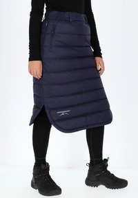 Merellinen paksu eristetty hame vaakasaumalla, sivutasku vetoketjulla ja logotunnus. Yhdistettynä mustiin leggingseihin ja tukevisiin mustiin saappaisiin.