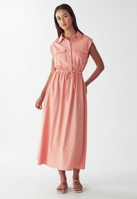 Maxime dress in soft coral fabric, jossa on napitettava etuosa, lyhyet hihat, kaksi rintataskua ja elastinen vyötärö nauhalla.