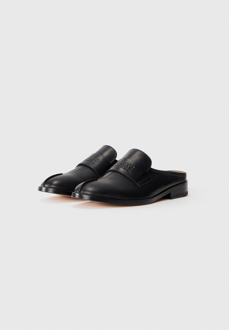 Svarta läderskor med låg klack, med rundad tå och bred rem över mellanfoten. Slät yta och minimalistisk design.