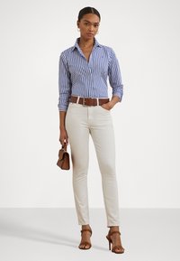 Striped blue and white button-up shirt with rolled sleeves, paired with cream-colored fitted pants and brown belt. Brown handbag and heels.
