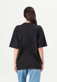 Black oversized t-shirt with short sleeves, crew neck, and smooth cotton material. Worn with light blue jeans. Back view shows no embellishments.