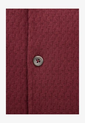 Bordowy dzianinowy materiał z teksturowanym wzorem i pojedynczym, okrągłym, czteroodkrytym, przezroczystym szarym guzikiem przyszytym w pobliżu środka.
