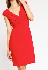 Vestido rojo hasta la rodilla con escote en V, mangas cortas y detalles fruncidos a lo largo del torso, hecho de una tela suave.