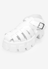 Sandalias anchas blancas hechas de un material brillante. Presentan correas estrechas, punta descubierta y una correa ajustable en el tobillo con una hebilla metálica.