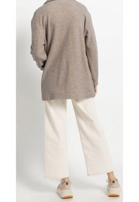 Maglione over-size color taupe chiaro con una consistenza morbida, abbinato a pantaloni a gamba larga di colore crema. Le sneakers sono beige con una suola a contrasto.