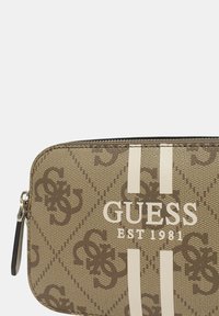 Pochette Guess marrone a fantasia con chiusura a zip, caratterizzata da strisce bianche e testo del logo "GUESS EST 1981." Realizzata in materiale sintetico testurizzato.