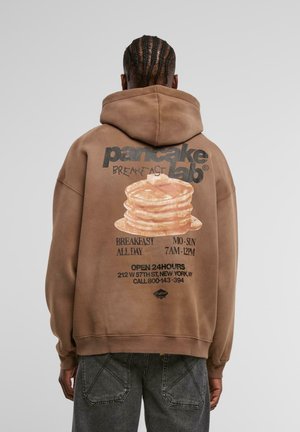 Felpa marrone con una grande grafica di pancake impilati con il testo: "pancake lab", "COLAZIONE TUTTO IL GIORNO" e dettagli sulla posizione in nero.